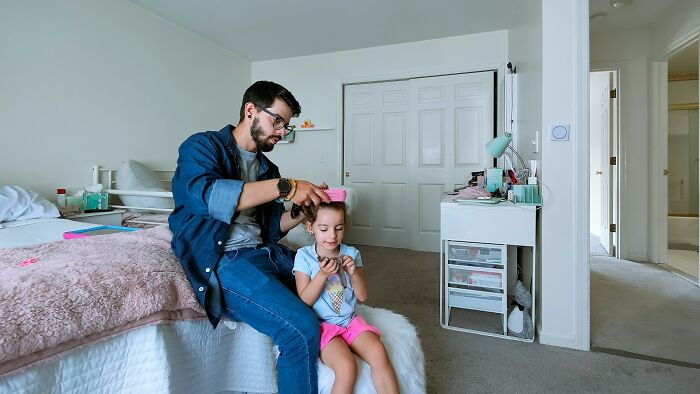 Father combing his daughter's hair in a cozy bedroom, highlighting moments of daily wins and family care.