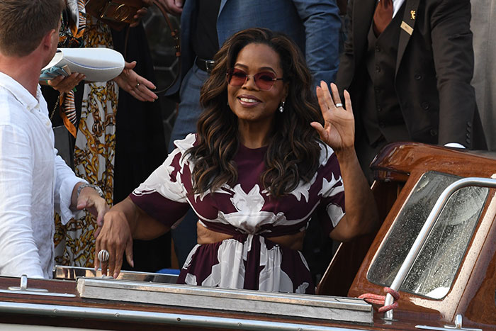Oprah smiling and waving while surrounded by people on a boat, controversial private road and tsunami access topic. - 4