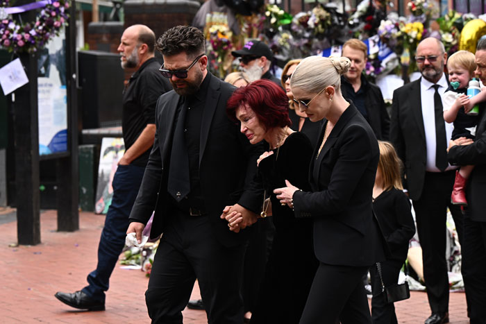 Sharon Osbourne tearful at Ozzy's funeral, supported by kids during a heartbreaking family farewell outdoors. Sharon Osbourne tearful at Ozzy's funeral, supported by kids during a heartbreaking family farewell outdoors.