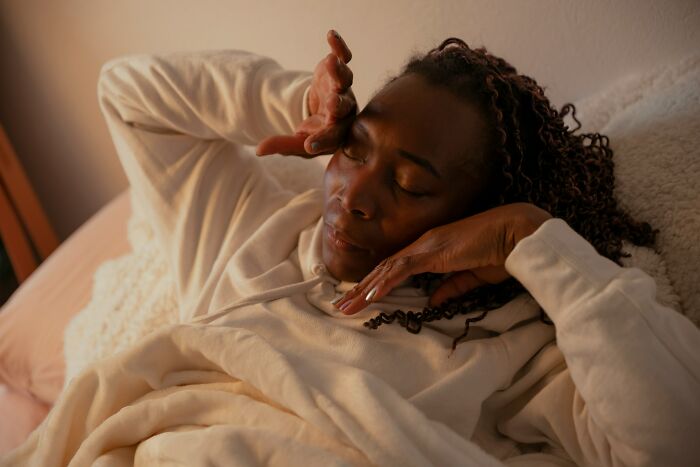 Woman resting in bed with eyes closed, showing signs of stress and fatigue related to toxic femininity behaviors. - 15