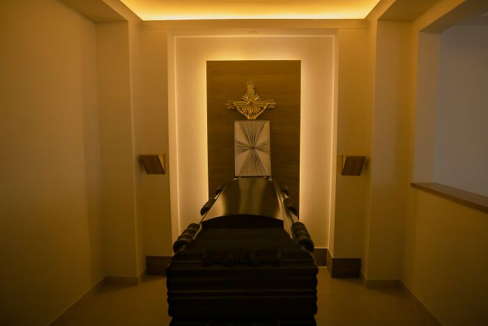 Coffin in a dimly lit room with a religious cross, illustrating the eerie details people who deal with dead bodies encounter.
