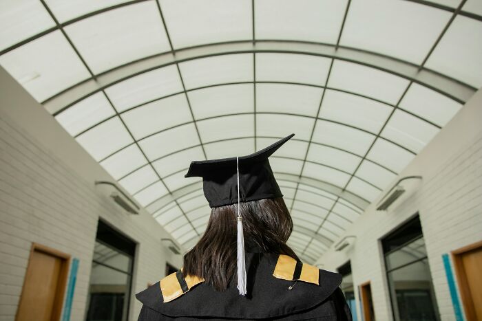 Graduate in cap and gown walking under a large glass ceiling hallway, symbolizing travelers sharing surprising things about the U.S.