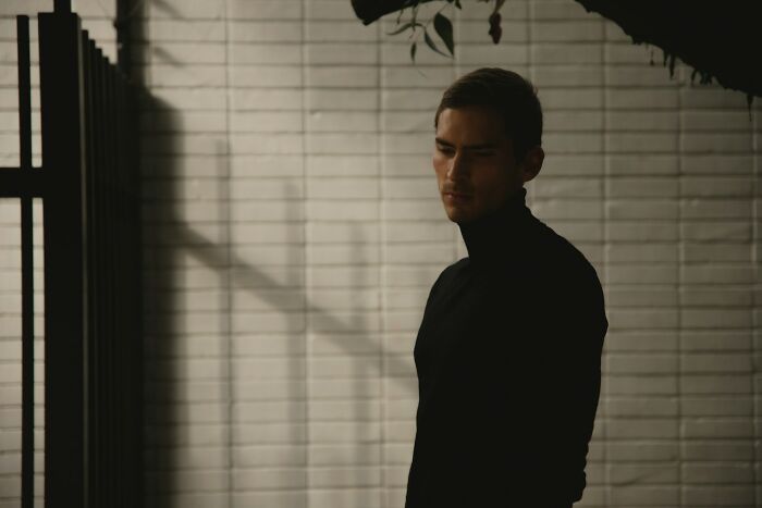 A private investigator in a black turtleneck stands in a dimly lit room, reflecting on unusual investigation cases. - 24
