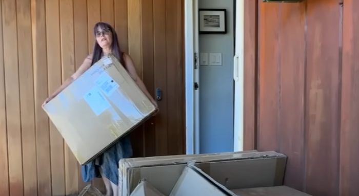 Woman holding large Amazon package at home with multiple mistakenly delivered Amazon packages stacked nearby. Woman holding large Amazon package at home with multiple mistakenly delivered Amazon packages stacked nearby.