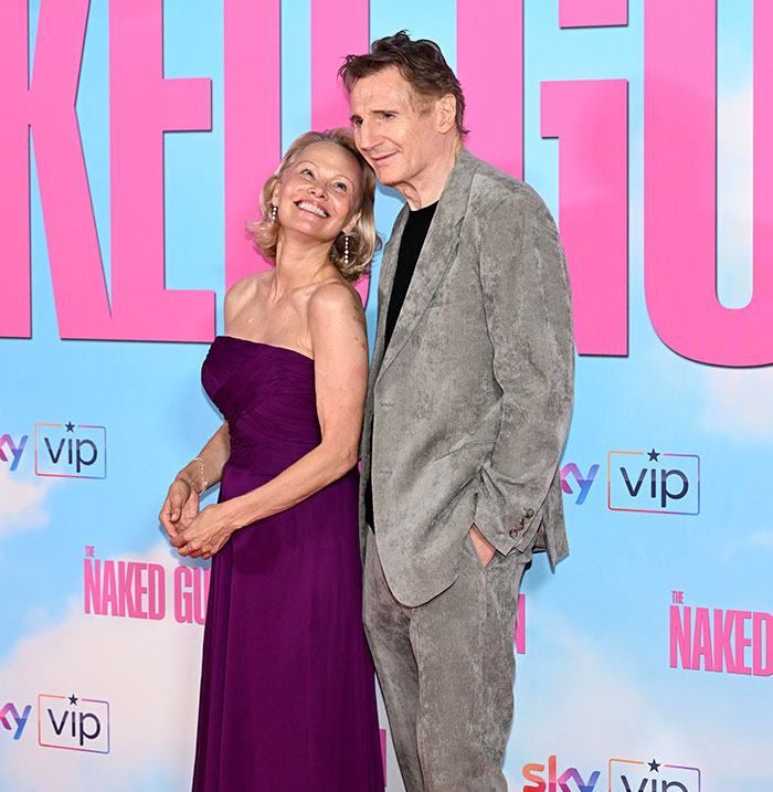Pamela Anderson and Liam Neeson posing together on the red carpet, smiling and showing affectionate body language. - 2