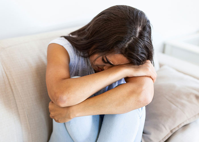 Woman sitting on couch, looking upset and stressed, reflecting on parents giving sister &pound;160K while she struggles financially