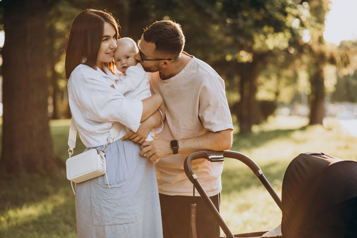 Young parents outdoors with baby and stroller, highlighting mom's overprotective feelings about in-laws helping with baby care.