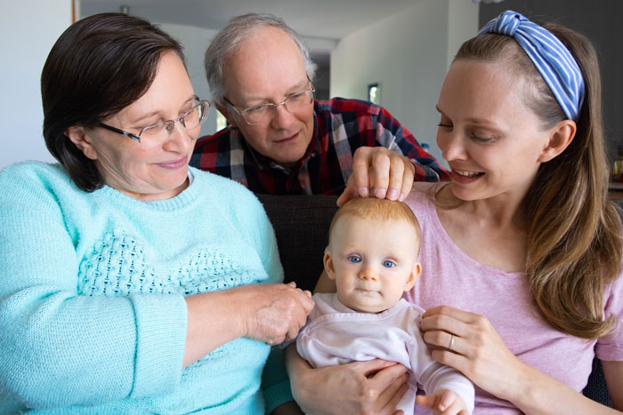 Mom with baby and in-laws helping care, showing overprotective family dynamics and mixed emotions.