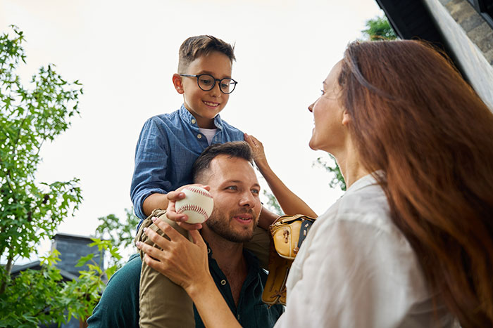 Father carries smiling son on shoulders holding baseball, while mother interacts closely, highlighting family favoring adopted kids over bio son. - 22