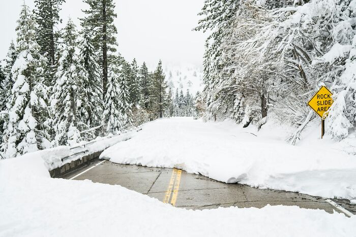 Snow-covered road blocked by a large snowdrift in a forested area, illustrating common debunked lies people believe about winter hazards.