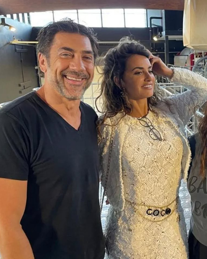 Woman in white dress with chain belt standing next to smiling man in black shirt at Paris Fashion Week event