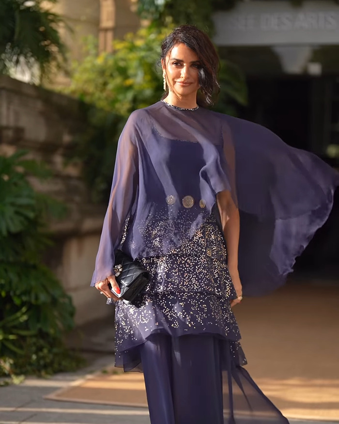 Pirates of the Caribbean actress at Paris Fashion Week wearing a flowing navy blue embellished dress and holding a black clutch.