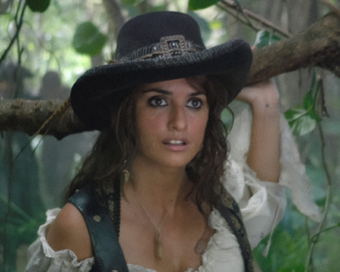 Legendary Pirates of the Caribbean actress wearing a black hat and pirate costume in a forest setting.