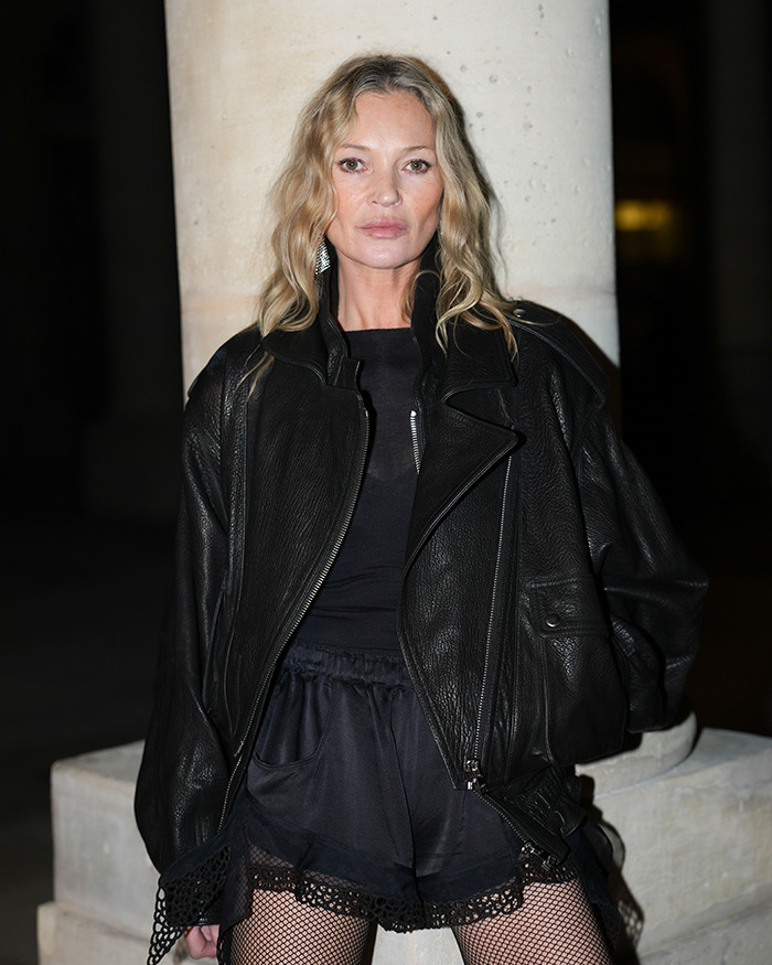 Kate Moss posing in a black leather jacket and fishnet stockings at a nighttime event, highlighting fashion style. - 1