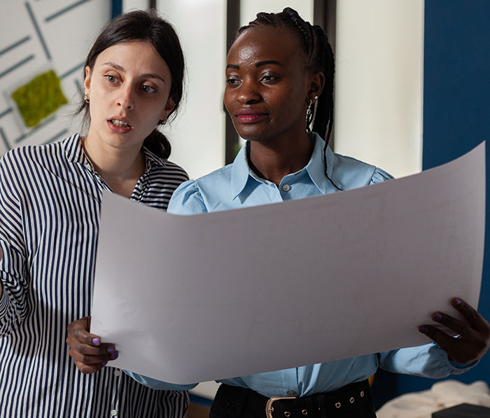 Two women examining large blueprint or plan, showing people had enough and took action together in discussion. - 15