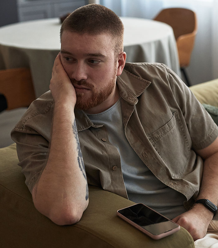 Young man looking frustrated and thoughtful on a couch with phone nearby, feeling he had enough and took action - 4
