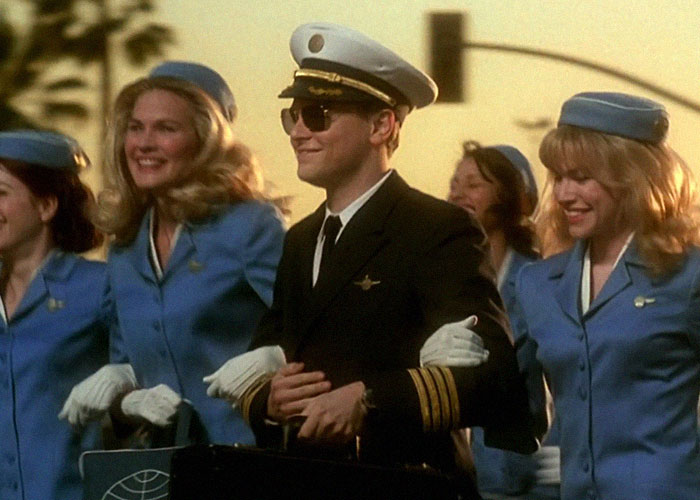 Scene from a movie showing a pilot with women in blue uniforms, illustrating people who went to school with celebrities.
