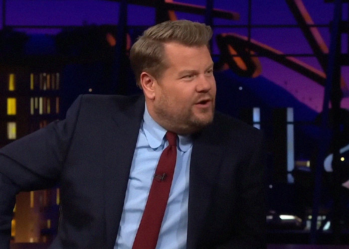 Man in a dark suit and red tie speaking on a talk show about people who went to school with celebrities.