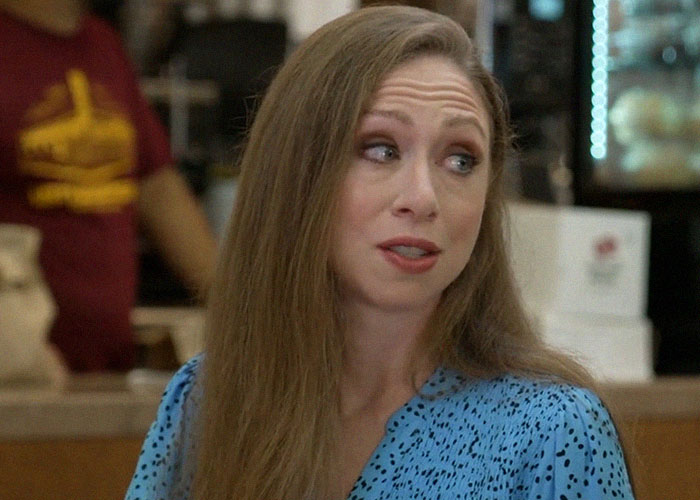 Woman with long hair wearing a blue polka dot shirt, sharing stories about people who went to school with celebrities
