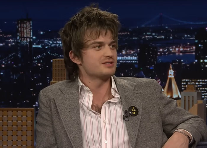 Young man in a gray blazer discusses experiences of people who went to school with celebrities on a late-night talk show.