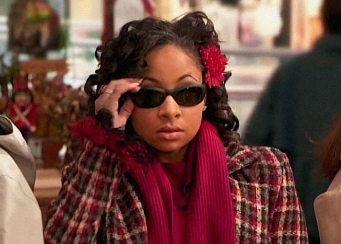 Young woman wearing dark sunglasses and a patterned coat, representing people who went to school with celebrities.