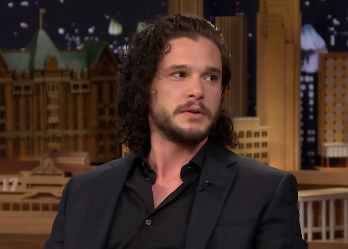 Actor with curly hair in a dark suit speaking during an interview about people who went to school with celebrities.