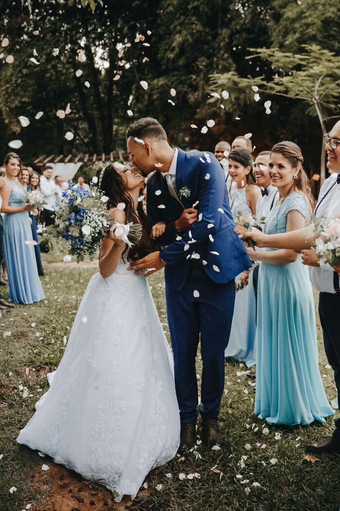 Bride and groom kissing outdoors with wedding party cheering, capturing moments of regret and gut feeling ignored celebration.