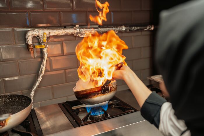 Person ignoring their gut feeling while cooking as flames flare up from a pan on a gas stove, risking a fire hazard.