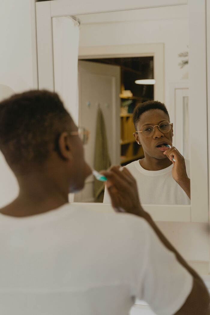 Person brushing teeth in front of a bathroom mirror reflecting a thoughtful expression, symbolizing relationship red flags. - 29