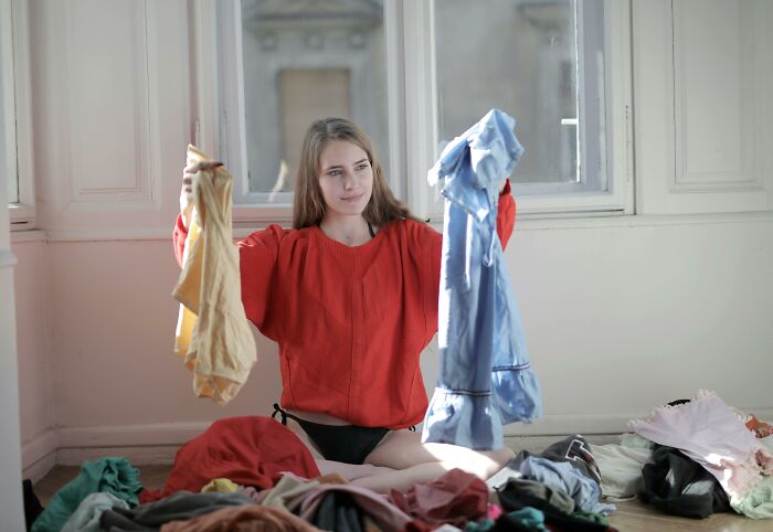 Young woman sitting on floor holding clothes, surrounded by messy laundry, illustrating partner needing a parent relationship red flag. - 12