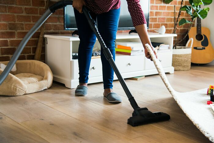 Person vacuuming hardwood floor while lifting a rug, illustrating a huge red flag in a relationship needing parenting. - 3