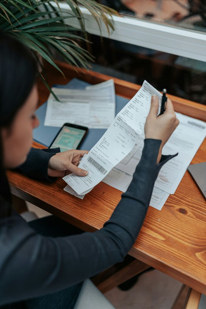 Person reviewing receipts and bills at a wooden desk, illustrating a relationship red flag about needing a parent not a partner. - 19