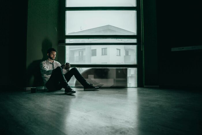 Young man sitting alone on the floor by a large window, reflecting on sad brutal and discouraging truths about life. - 3