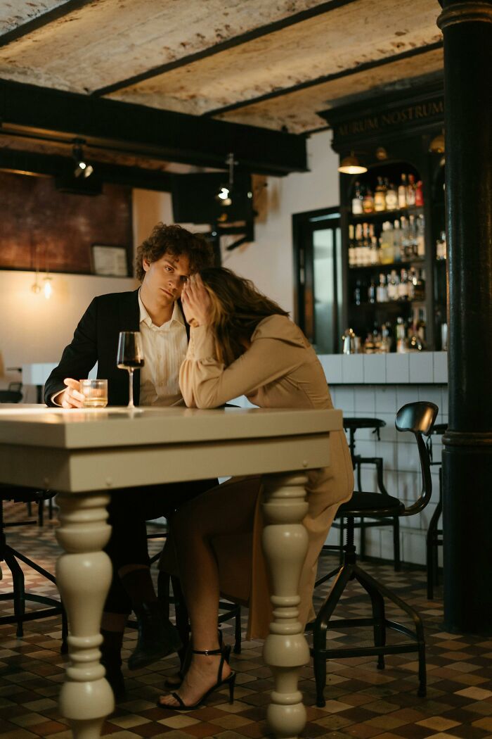 A couple sitting at a bar table, woman upset covering her face, reflecting sad brutal and discouraging truths about life. - 19