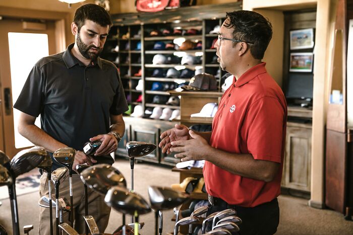 Two men discussing golf clubs in a shop, conveying a moment reflecting on sad brutal and discouraging truths about life. - 32