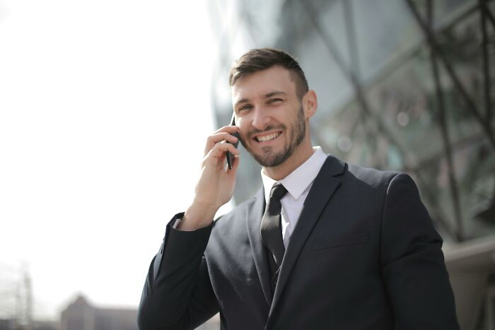 Smiling man in a suit talking on phone outdoors, representing psychology experiments and human behavior insights.