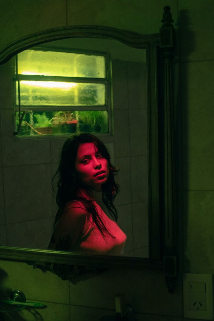 Woman with red light reflection looking in an old mirror, illustrating concepts from psychology experiments on perception and self-awareness.