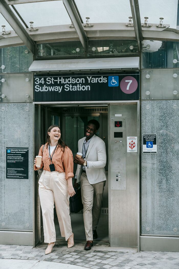 Two professionals exiting 34 St-Hudson Yards Subway Station, smiling and holding coffee, illustrating psychology experiments.