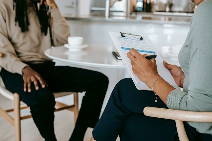 Person conducting psychology experiments, taking notes on a clipboard while interacting with another individual in a casual setting.