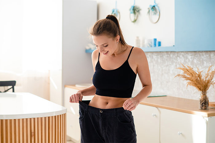 Young woman in a black top showing loose pants, illustrating the impact of loved ones taking Ozempic on weight changes.