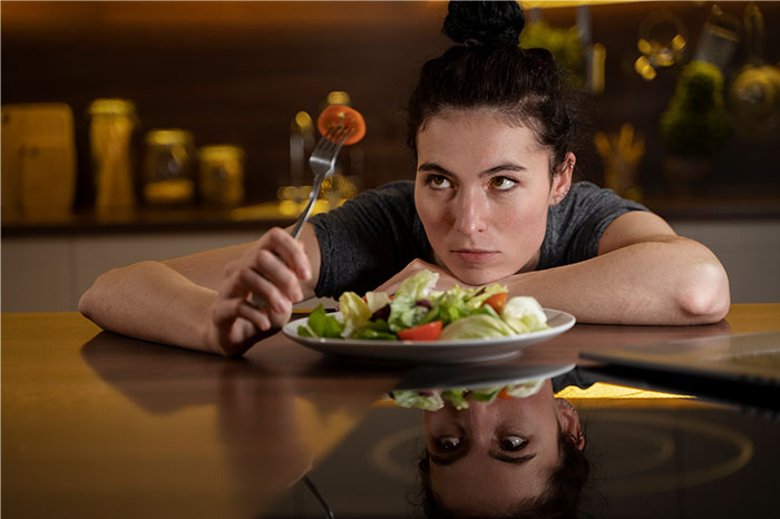 Young woman looking frustrated while holding a fork over a salad, reflecting on loved ones taking Ozempic.