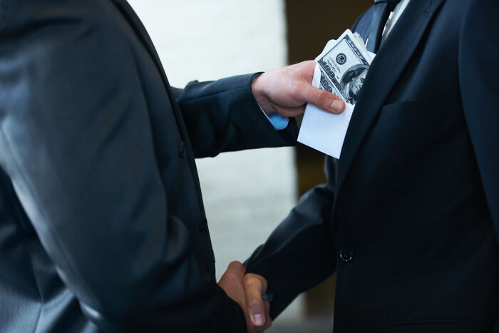 Two businessmen shaking hands while one secretly slips cash in an envelope, illustrating company secrets from customers. - 30