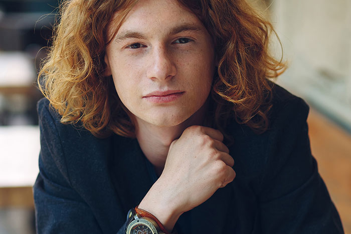 Young worker with curly red hair wearing a dark jacket, showing confidence after calling out their boss at work.