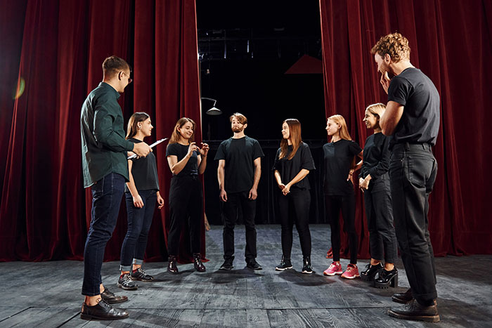 Group of workers standing in a theater setting, discussing and preparing courageously to call out their bosses.