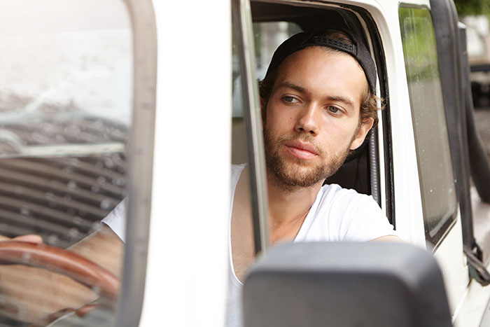 Young man wearing a backward cap sitting in a vehicle, reflecting after calling out his boss at work.