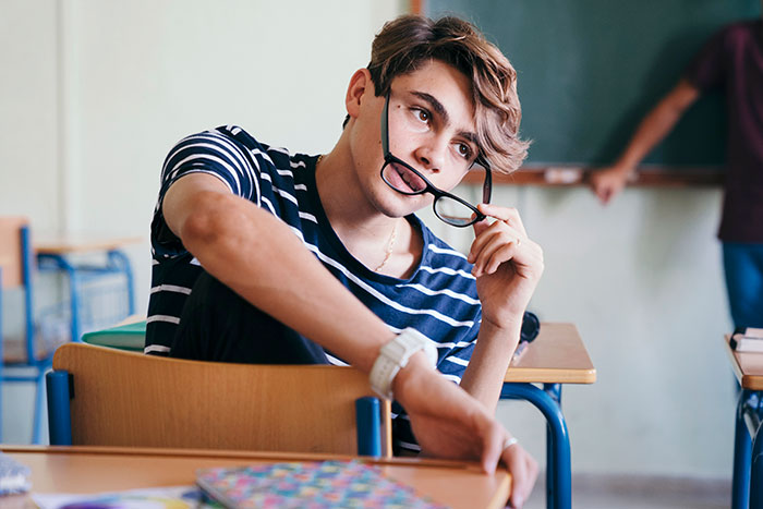 Young man with striped shirt holding glasses thoughtfully in a classroom, representing workers who called out their bosses.