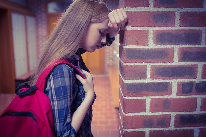 Young worker leaning against a brick wall, showing stress and courage after calling out her boss at work.