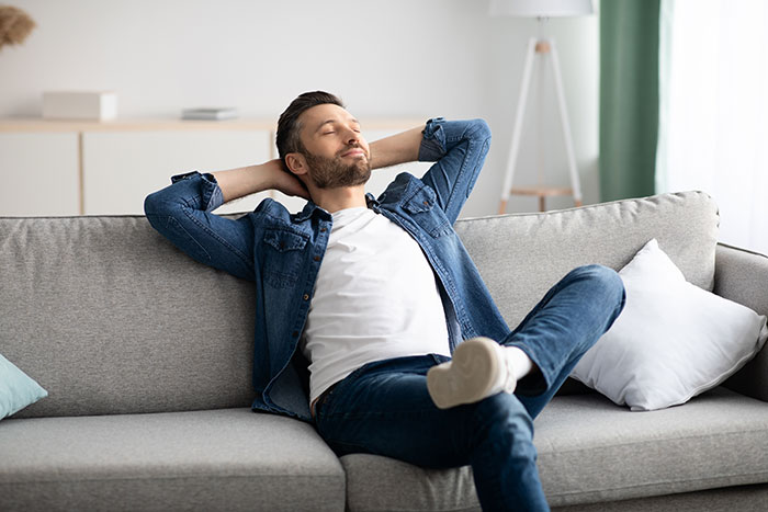Man relaxing on couch at home, expressing refusal to act as landlord for sister and her family.