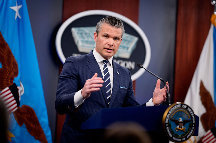 Pete Hegseth speaking at a podium in a suit with Department of Veterans Affairs flags in the background.