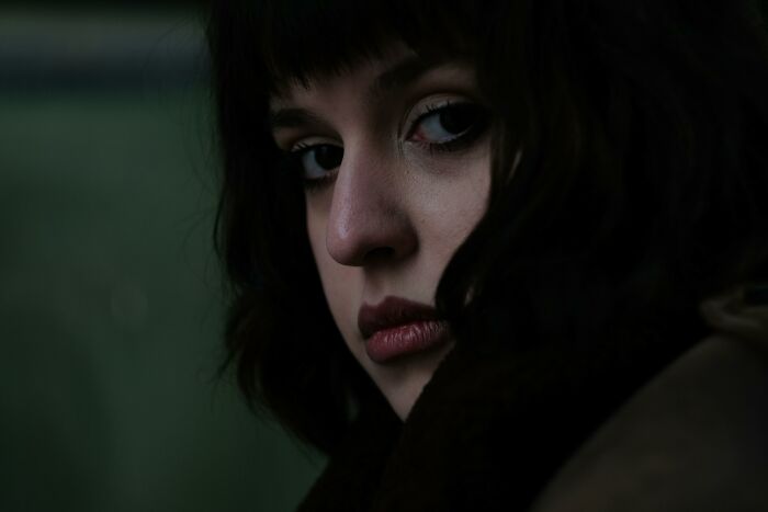 Young woman with dark hair looking pensively in low light, evoking neighbor tales that might inspire moving to the woods.